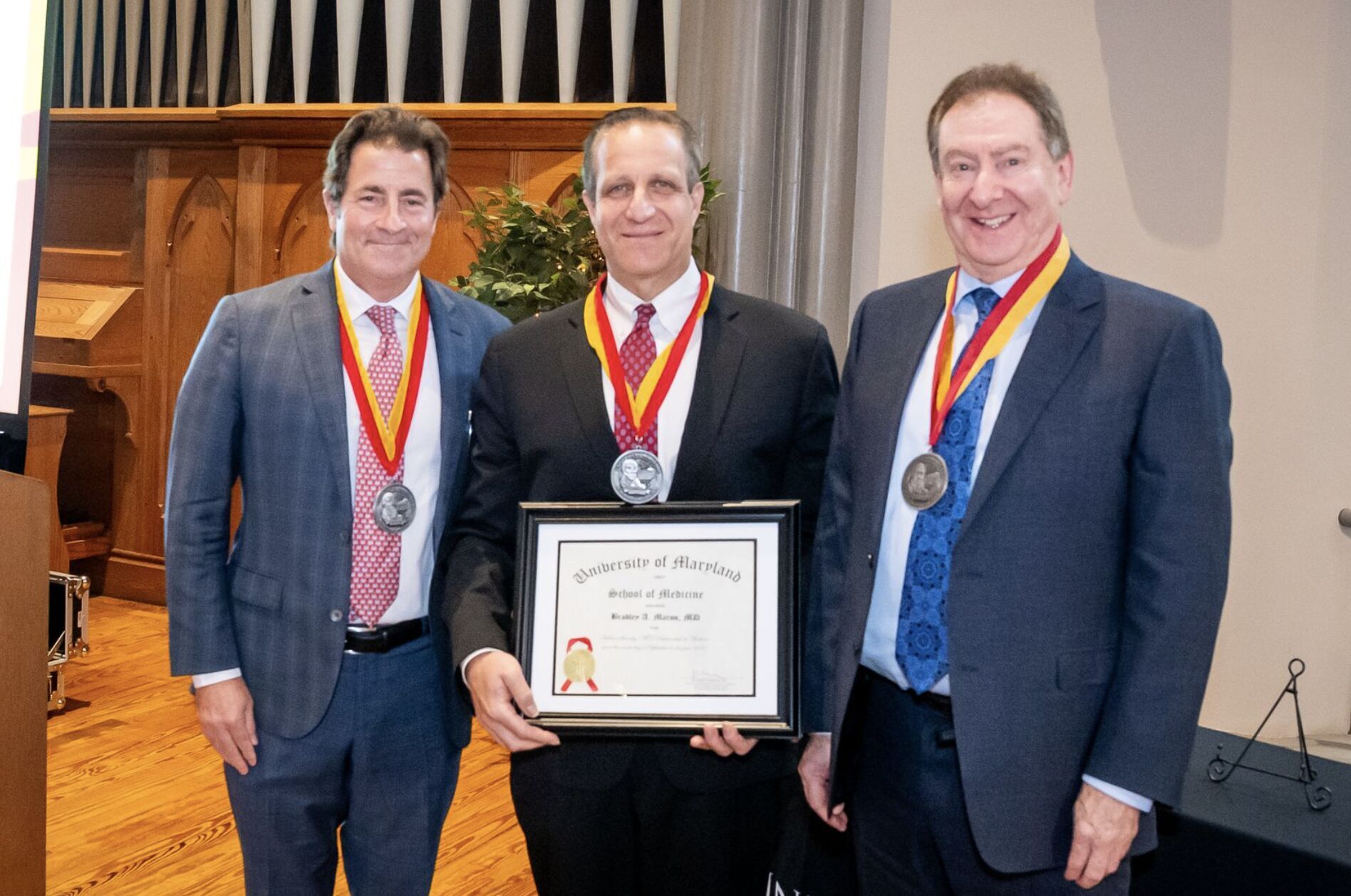 Three men standing together. Man in the middle holding an award.
