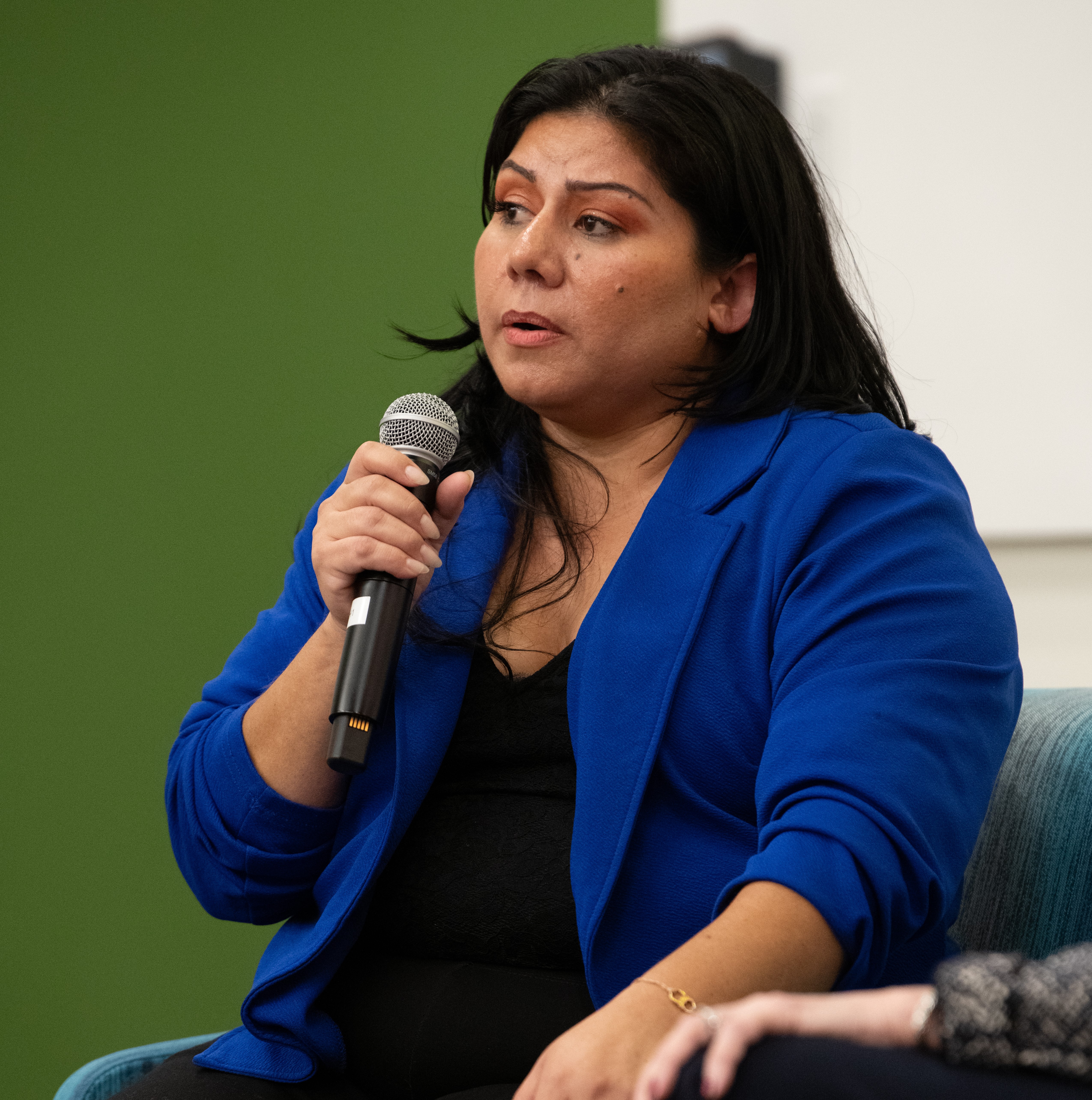 Woman in a blue blazer speaks into a microphone.