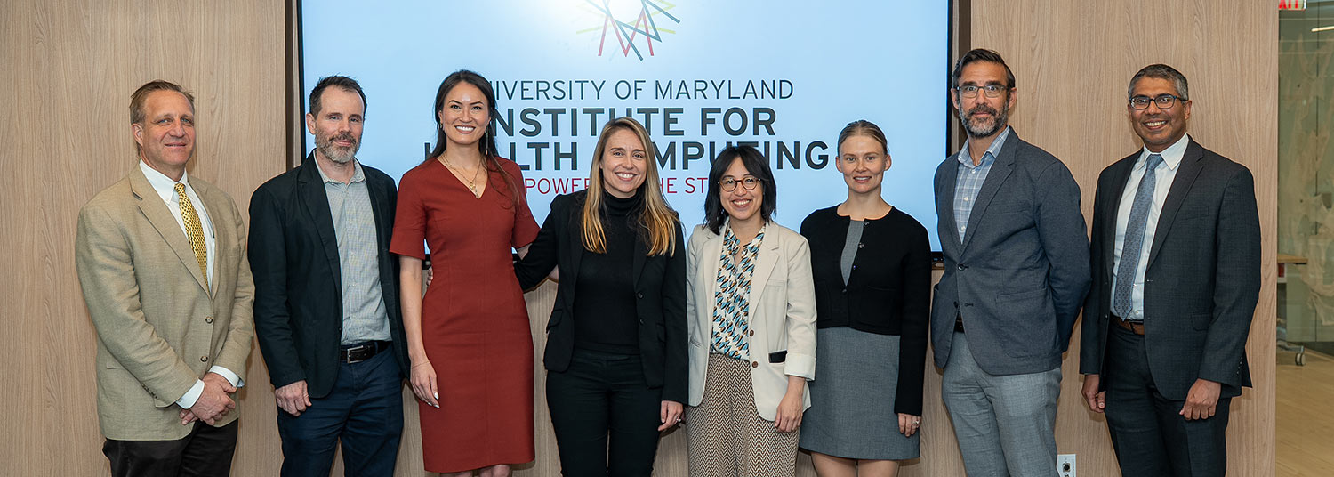Four men pictured with four women in front of a screen with UM-IHC logo.