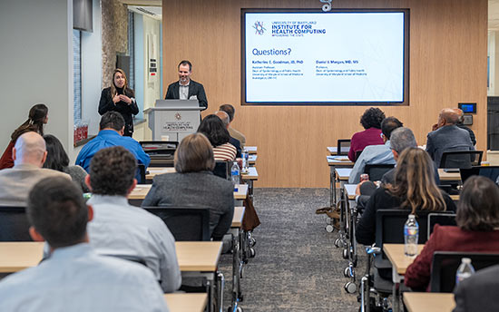 Female panelist at podium in front of the room speaks to the audience.