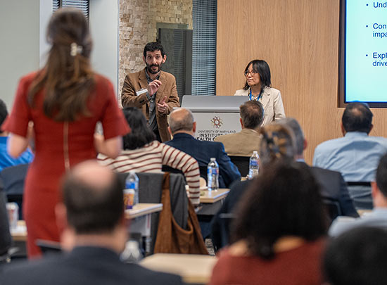 Female audience members stands to ask a question of two panelists at the podium.