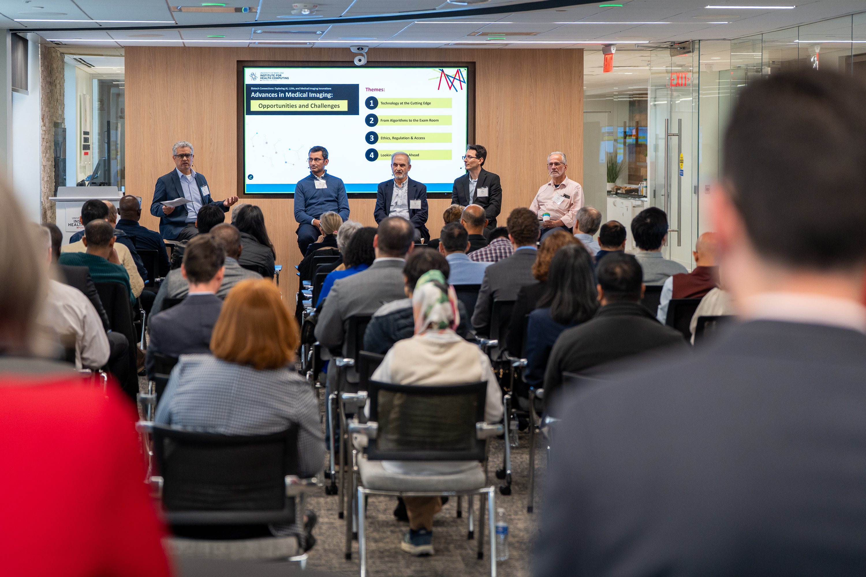 A room full of attendees, seated in front of a panel of five men.