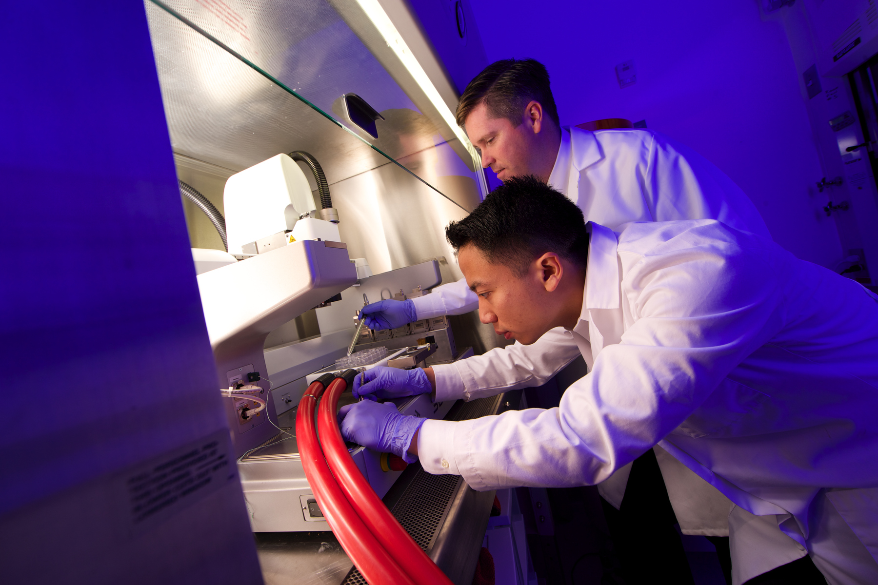 Two males pictured in a lab with purple lighting in the background.