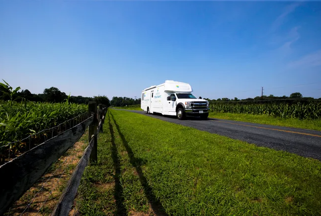 Mobile clinic driving on a road sandwiched between corn fields.